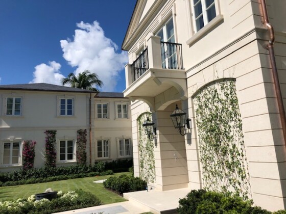 Elegant beige mansion with climbing ivy and a manicured lawn under a blue sky.