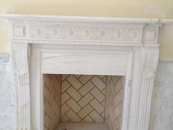 Elegant white marble fireplace with intricate carvings and herringbone tile interior.