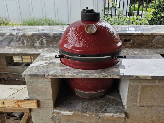 A red ceramic kamado grill embedded in a stone countertop.