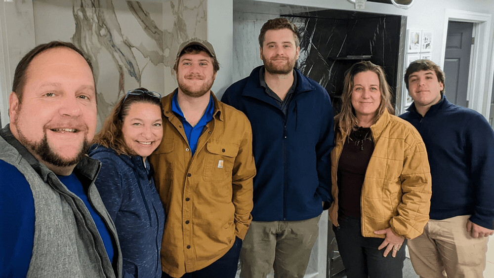 Group of six people smiling indoors in casual attire.