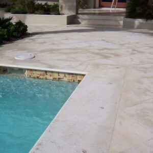 Close-up of a clean pool edge with tiled waterline and beige stone decking.