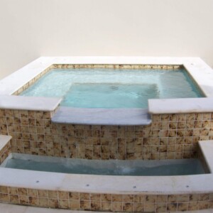 Elegant tiled hot tub with a small water feature in a minimalist setting.
