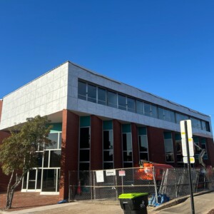 Modern two-story building with large windows and a fenced exterior under a clear blue sky.