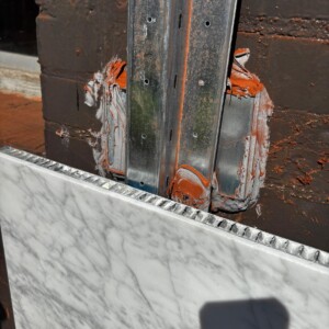 Damaged wall with exposed metal studs and peeling paint behind marble panel.