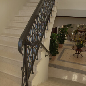 Elegant staircase with intricate wrought iron railing in a spacious, tastefully decorated home.