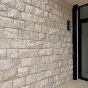Wall made of light-colored rectangular stone bricks with a black pipe and glass door on the right.