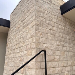 Modern building corner with beige stone brick wall and black railing.