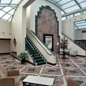 Elegant lobby with marble floors, stairs, and floral centerpiece under a glass ceiling.