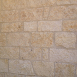 Beige stone wall with rough texture and rectangular blocks.