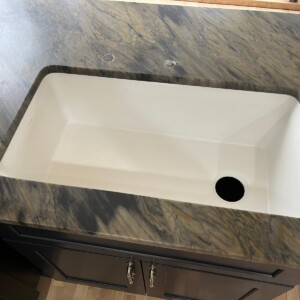 Rectangular white sink installed in a marble countertop with dark cabinetry below.