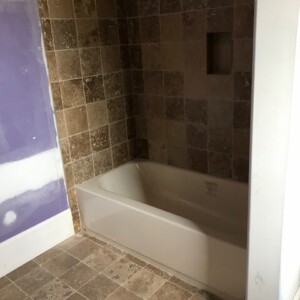 Bathtub surrounded by brown tiled walls and floor in a partially painted bathroom.