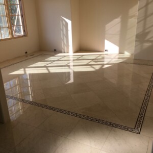 Empty room with polished marble floor and decorative border reflecting sunlight.