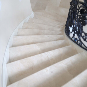 Curved marble staircase with ornate black railing.
