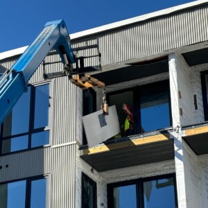 Construction worker uses crane to lift building materials to upper floor balcony.