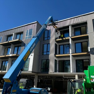 Construction workers use a blue boom lift to work on an apartment building exterior.
