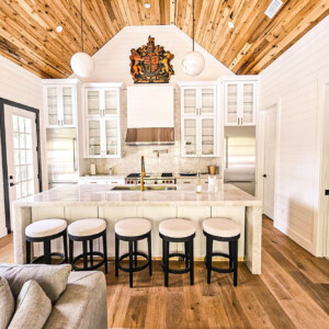 Modern kitchen with white cabinetry, marble island, and wooden ceiling.