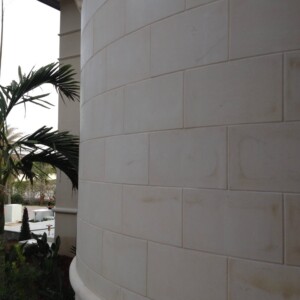 Curved beige block wall with tropical plants in the background.