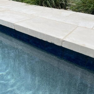 Close-up of a pool edge with clear water and stone tiles.