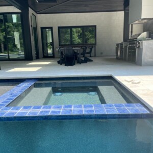 Modern outdoor pool area with a blue-tiled spa and kitchen.