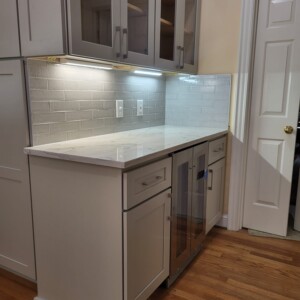 Modern kitchen counter with white cabinets, marble countertop, and glass-front wine cooler.