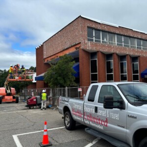 Workers on a lift repairing a building facade with a branded truck nearby.