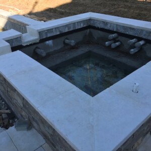 Empty stone and concrete water feature with pipes, under construction outdoors.