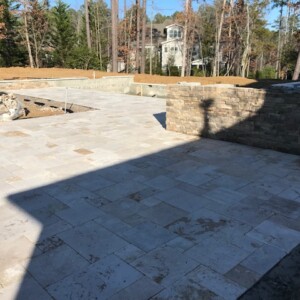 Newly paved stone patio with surrounding stone wall under clear sky.
