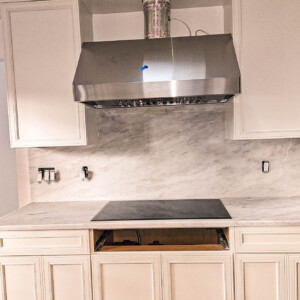Modern kitchen setup with marble backsplash and stainless steel range hood.