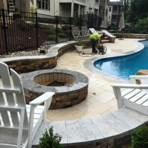 Outdoor pool area with fire pit, white chairs, and person working.
