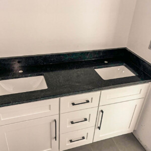Newly installed black countertop with dual sinks on white cabinets in a bathroom.