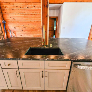 Modern kitchen island with black sink and gold faucet.