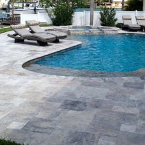 Silver travertine paver versailles pattern patio pool coping San Jose Califronia Modern poolside with lounge chairs and stone tiles near a waterfront.