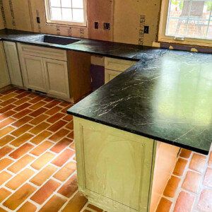 New kitchen installation with black countertops and brick-patterned floor tiles.