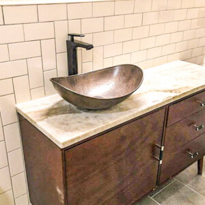 Modern bathroom vanity with a hammered copper sink and matte black faucet.