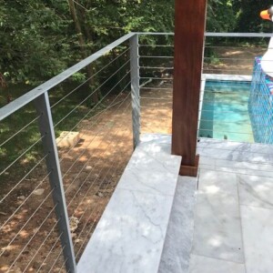 Modern outdoor railing with metal cables and marble seating near a pool.