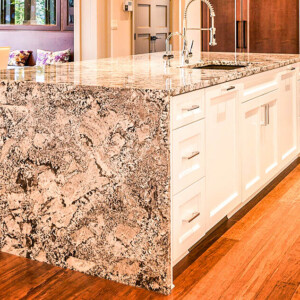 Kitchen island with granite countertop and white cabinets on wooden floor.