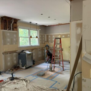 Room under renovation with construction tools and a worker preparing the floor.