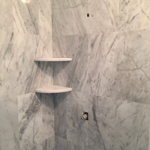 Corner marble shelves installed on marble tiled wall in a bathroom.
