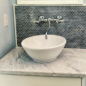 Modern bathroom sink with marble countertop and mosaic backsplash.