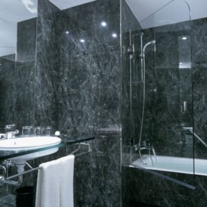 Modern bathroom with dark marble walls and glass shower enclosure.
