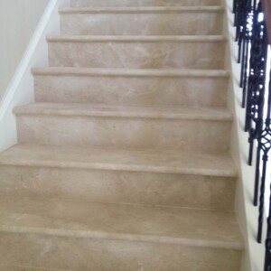 Beige marble stairs with black wrought iron railing.