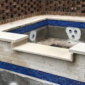 Partially constructed pool with blue tile accents and brick wall background.