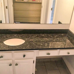 Bathroom vanity with black granite countertop and white cabinets.