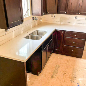 Newly installed white countertop with dark wood cabinets in kitchen under renovation.