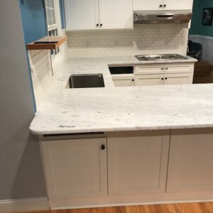 White kitchen with marble countertops and a stainless steel sink.