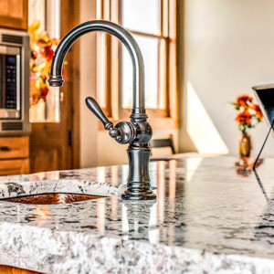 Island sink and granite countertops Elegant black kitchen faucet on a polished granite countertop with natural light.