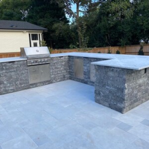 Outdoor kitchen with stone countertops and built-in grill on tiled patio.