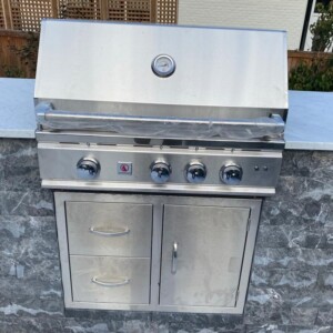Stainless steel built-in outdoor gas grill with control knobs and storage compartments.